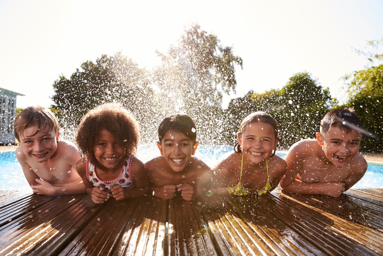 多个孩子笑着笑着，在室外游泳池与飞溅的水玩得很开心＂title=