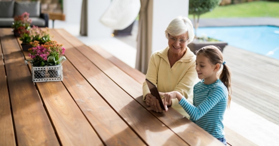 孙女和祖母在甲板遮阳处用平板电脑讨论＂height=
