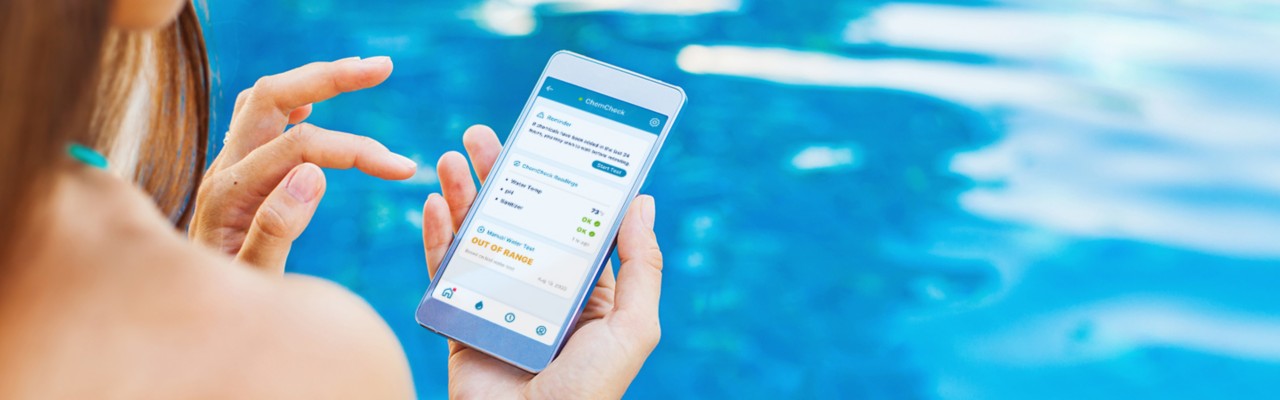 一个女人坐在泳池边，在手机上显示水里的化学反应，泳池自动化＂title=