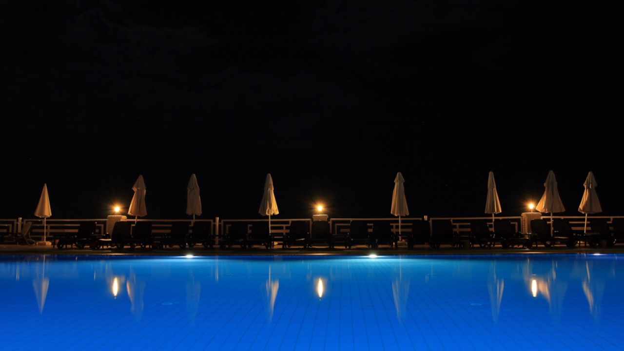夜间照明室外游泳池与封闭的沙滩椅伞＂class=