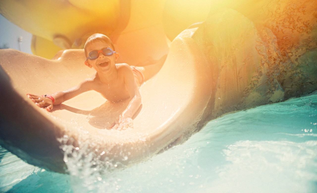 小男孩在滑水道上滑。这个5岁的有趣男孩戴着泳镜。马略卡岛阳光明媚的夏日。