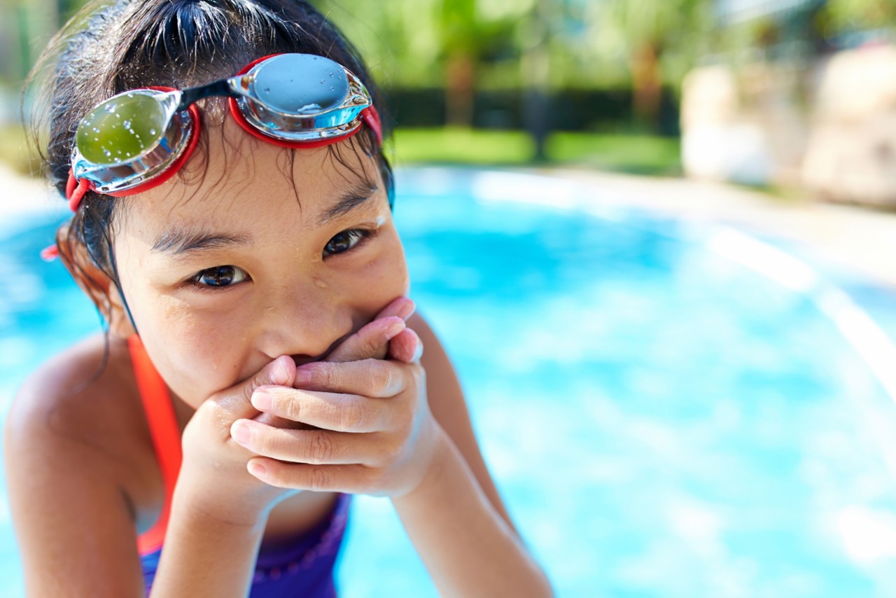 一个可爱的亚洲小女孩在游泳池对着相机微笑的特写＂class=
