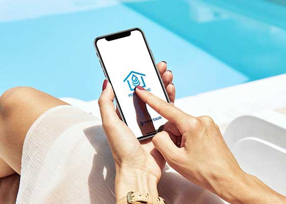 女人在电话旁边用Pentair Home应用程序清除蓝色泳池＂class=