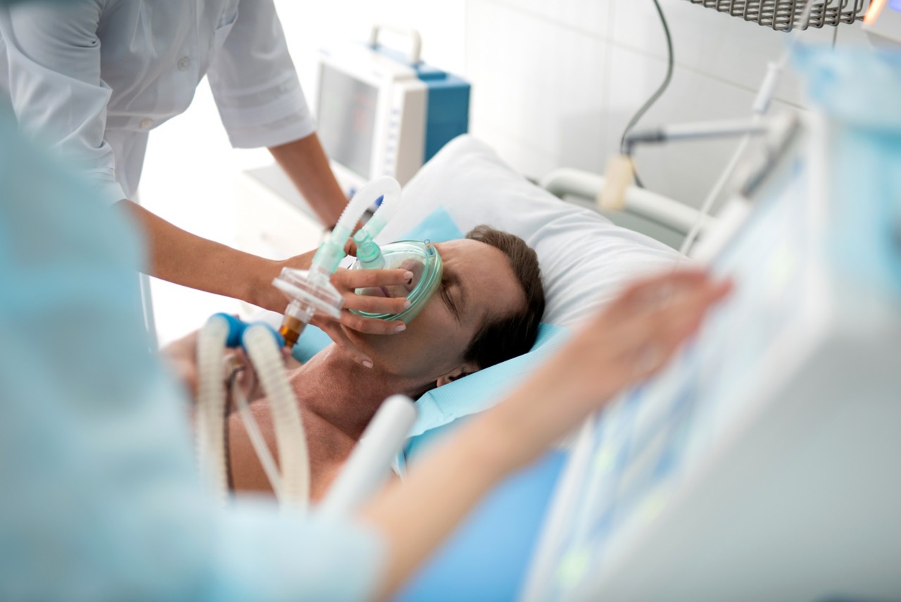 昏迷的中年男子在医院接受机械通气，女性双手使用呼吸设备的特写＂class=