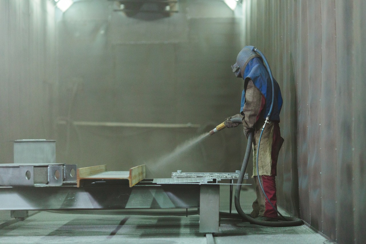 喷砂。金属爆破。一名员工准备一个金属零件进行喷漆。一个严厉的人在工厂工作。＂class=