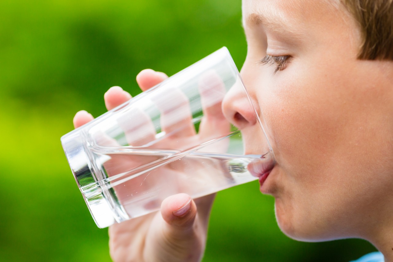 一个年轻的斯堪的那维亚孩子用模糊绿色背景的玻璃喝新鲜纯净的自来水。＂title=